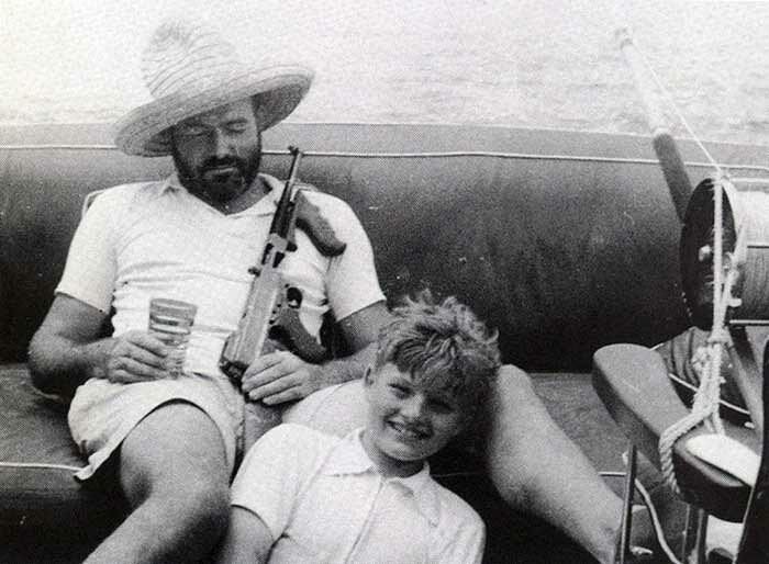 Эрнест Хемингуэй отдыхает в своей лодке с пистолетом-пулеметом Томпсона и сыном Джеком знаменитости, исторические фотографии, история, редкие фотографии, фото