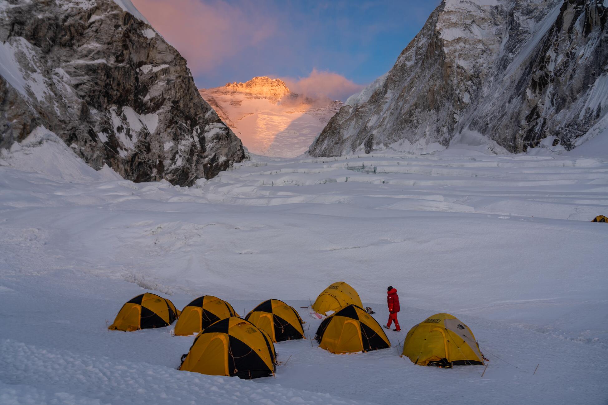 Picture of seven yellow and black tents in a group on a snow and ice covered field with the walls of Mount Everest behind them