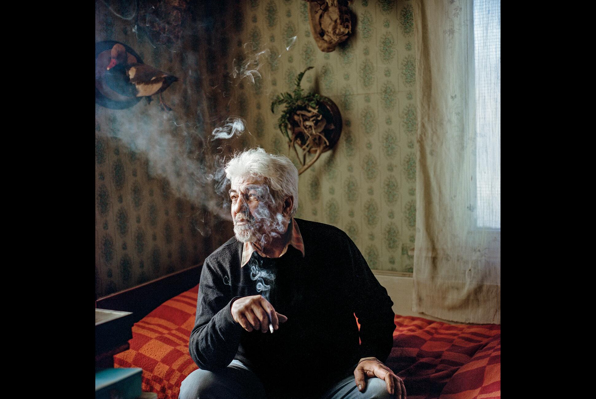 Фотография мужчины, курящего сигарету, сидя на кровати