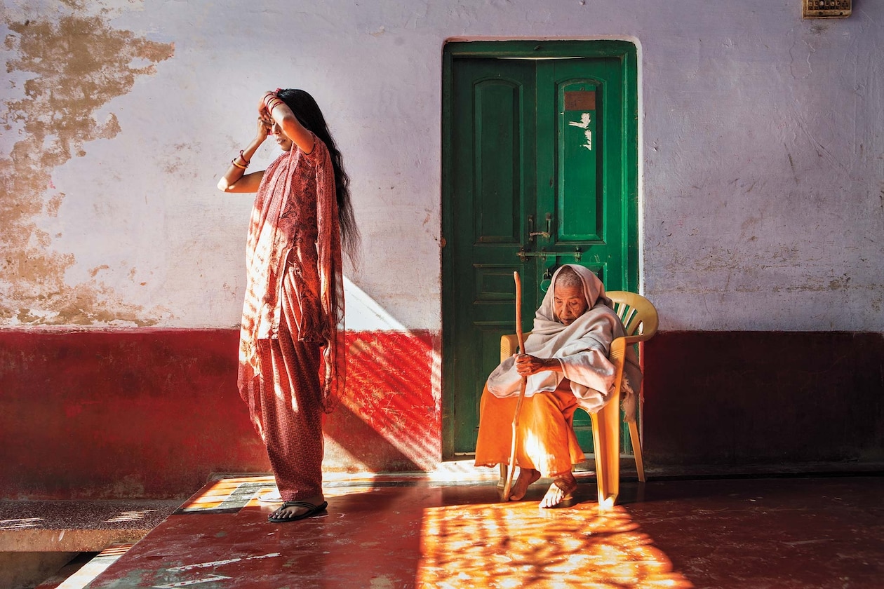 Женщина, стоящая и женщина, сидящая у зеленой двери, - вдовы в приюте