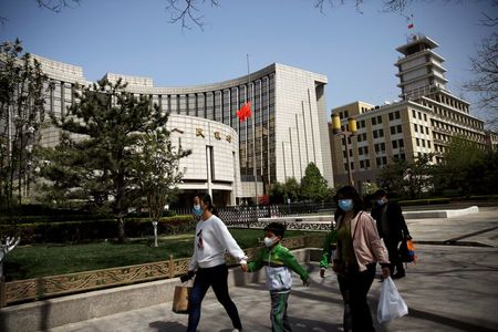 People wearing face masks walk past the headquarters of Chinese central bank People's Bank of China (PBOC), where the Chinese national flag flies at half mast in Beijing as China holds a national mourning for those who died of the coronavirus disease (COVID-19), on the Qingming tomb-sweeping festival, April 4, 2020. REUTERS/Tingshu Wang