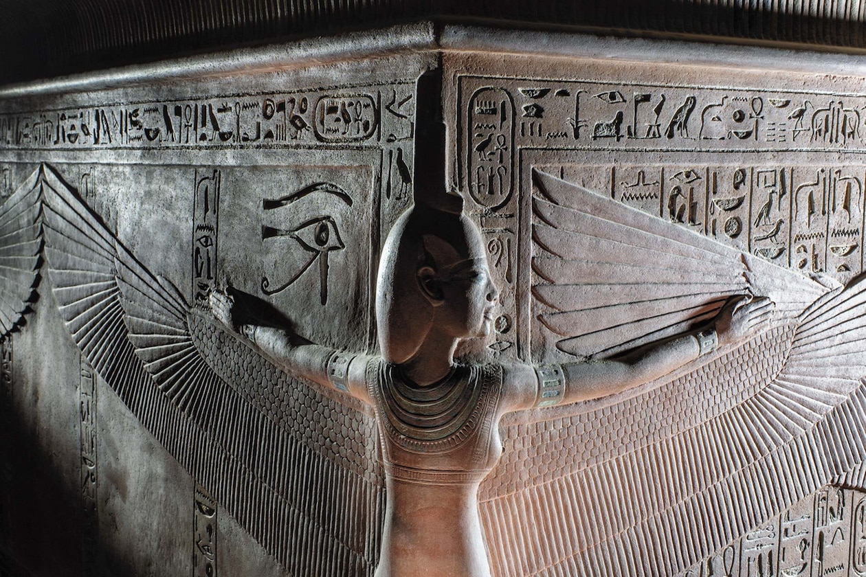 Вырезанный из камня древнеегипетский бог с крыльями, окруженный иероглифами