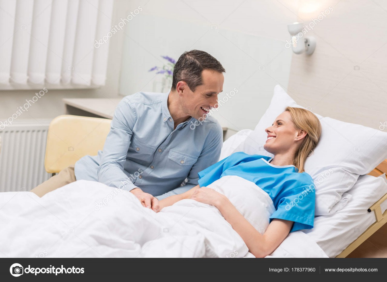 Близко навестить. Мужчина навещает в больнице. Муж у кровати жены в больнице. Жена навещает мужа в больнице. Девушка навещает в больнице.