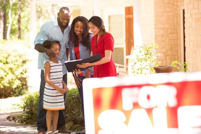A couple and child speaking with agent outside a home for sale.