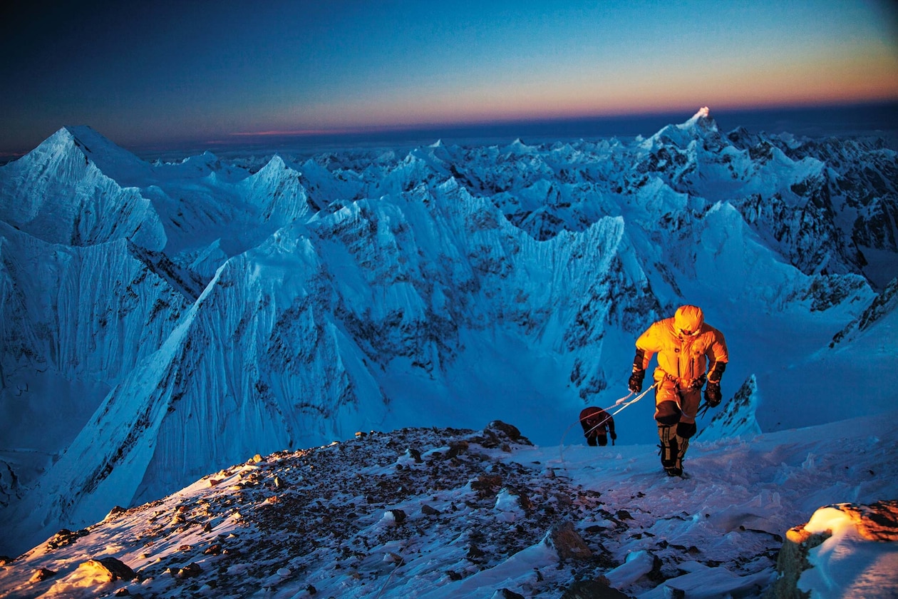 Два альпиниста, один в желтом, на вершине заснеженного пика