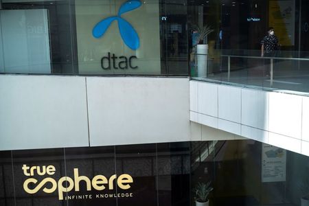 FILE PHOTO: A man walks next to the logo of the DTAC Public Company Limited and the logo of True Corporation at a department store in Bangkok, Thailand, November 22, 2021. REUTERS/Athit Perawongmetha/File Photo 