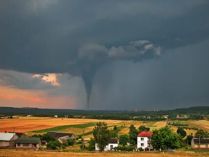A tornado behind a row of farmhouses and fields. 