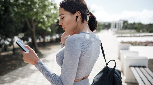 Молодая спортивная девушка слушает музыку на тренировке на улице