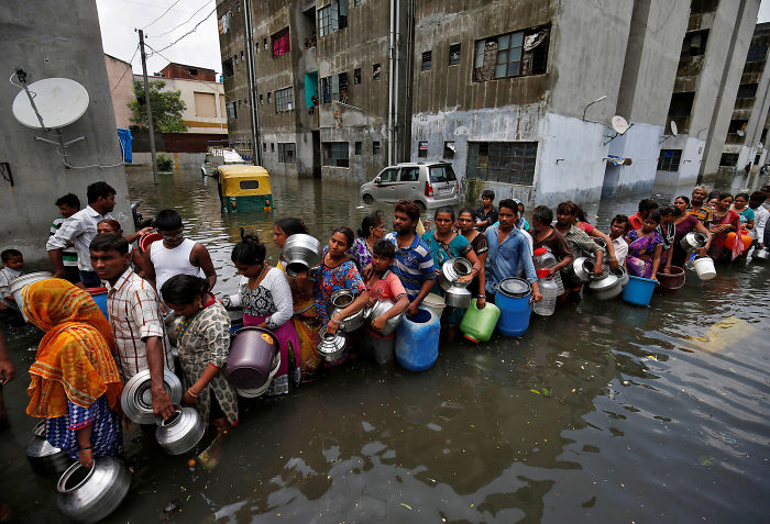 People Wait In A Line To Collect Drinking Water From A Municipal Tanker At A Flooded Residential Colony In Ahmedabad, India