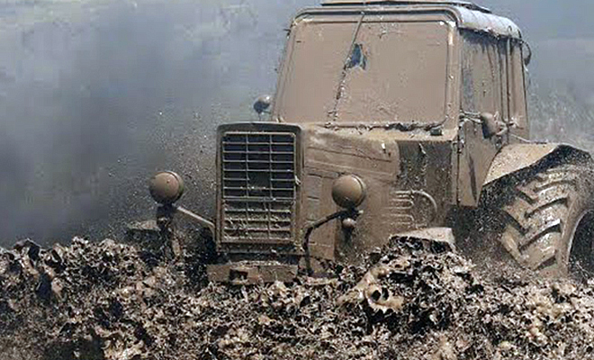 Выезд трактора из метровой грязи: тракторист использовал бревна на колесах. Видео