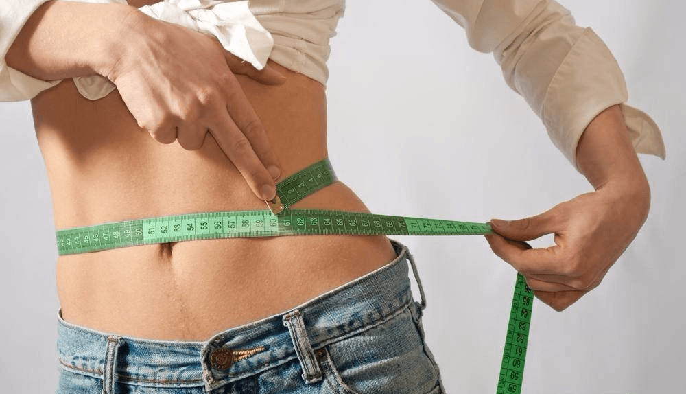 Девушка измеряет талию сантиметровой лентой