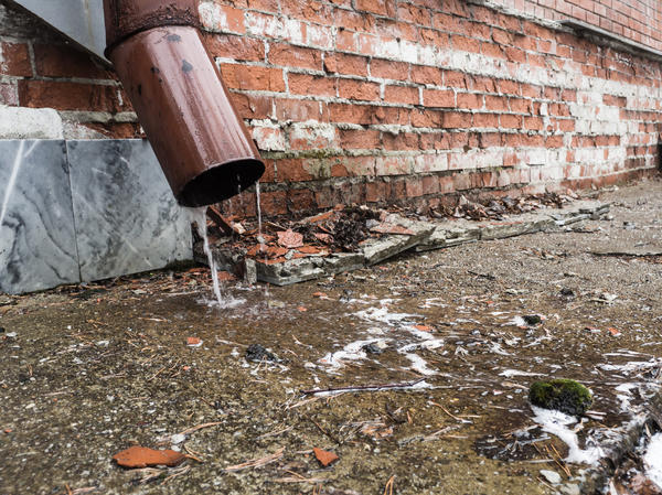 Текущая из водостока вода разрушает отмостку