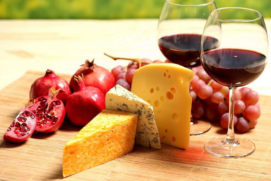 Вино в бокалах, сыр, гранат и виноград на столе