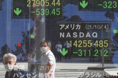 People wearing protective masks amid the coronavirus disease (COVID-19) outbreak are reflected on an electronic board displaying Japan's Nikkei and U.S. Nasdaq index outside a brokerage in Tokyo, Japan, October 5, 2021. REUTERS/Kim Kyung-Hoon