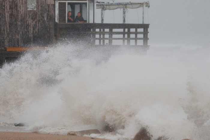 Люди смотрят, как волны разбиваются о бар Ocean Mist, когда тропический шторм Генри приближается к Южному Кингстауну, Род-Айленд