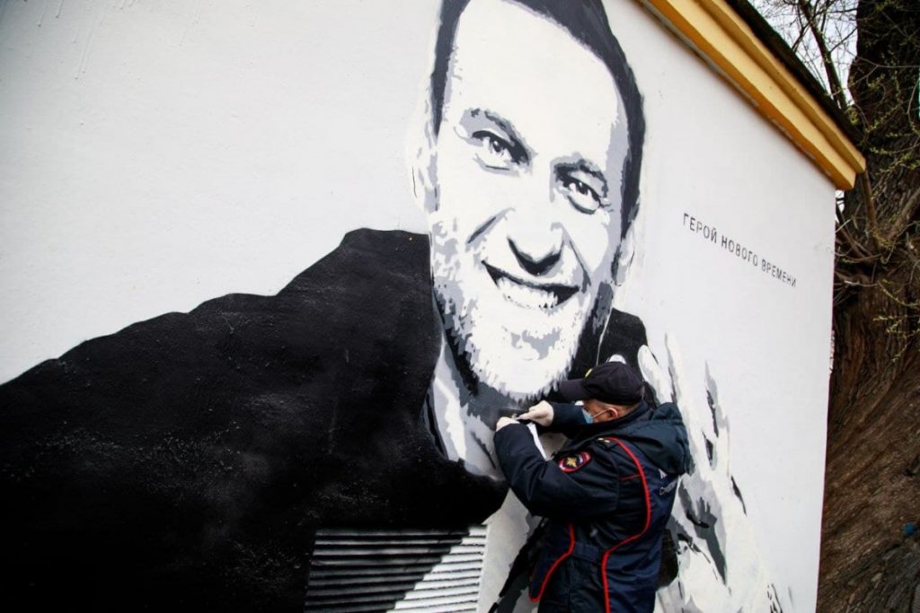 Сотрудник полиции соскребает краску с граффити Навального