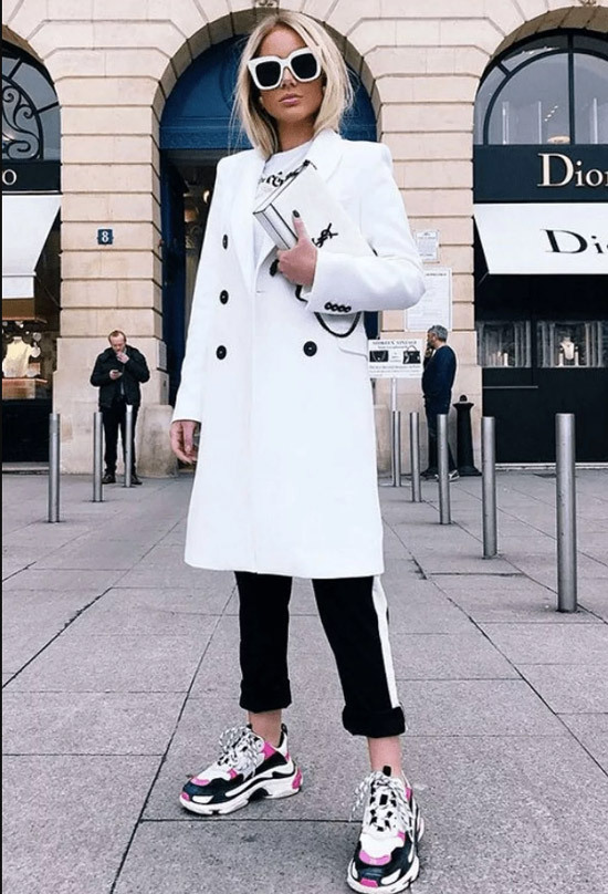 Девушка в белом пальто, черные брюки и кроссовки