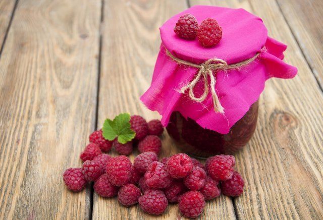 Raspberry jam with fresh raspberries on wooden background