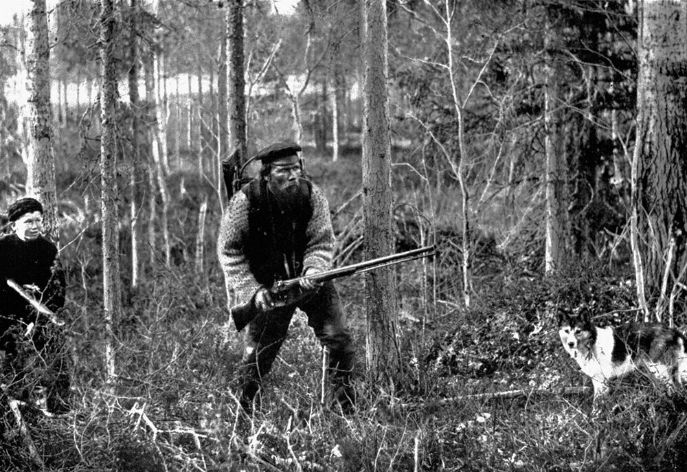 Охотник в Архангельской области, начало 20-го века. Фотография явно постановочная: охотник изображает, что напряженно вслушивается, как будто заметил впереди дичь. Однако поведение собаки выдает всю наигранность ситуации — она спокойно смотрит на фотографа...