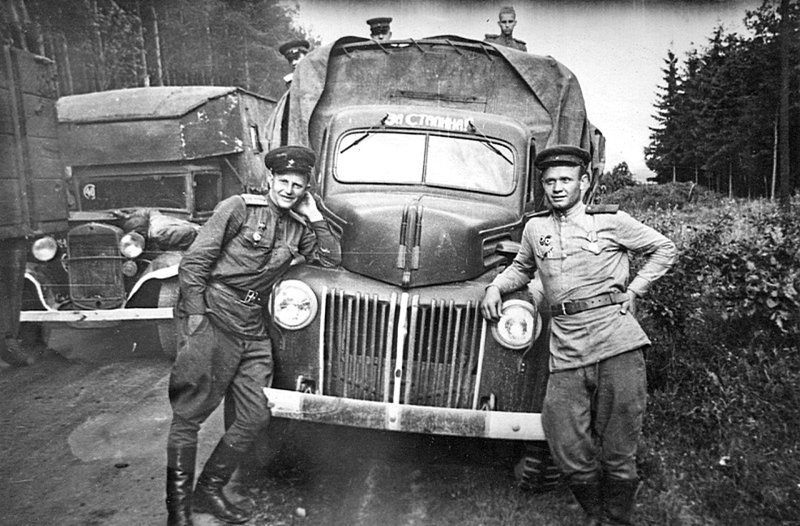Советские бойцы фотографируются у грузовика Форд (Ford G8T, американского производства, поставлялся по ленд-лизу в СССР) на обочине дороги во время отдыха. Слева — ремонтная мастерская на базе грузовика ГАЗ-АА. Время съемки: апрель - май 1945.