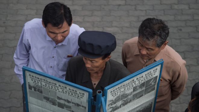 мужчины читают газету на улице в Пхеньяне