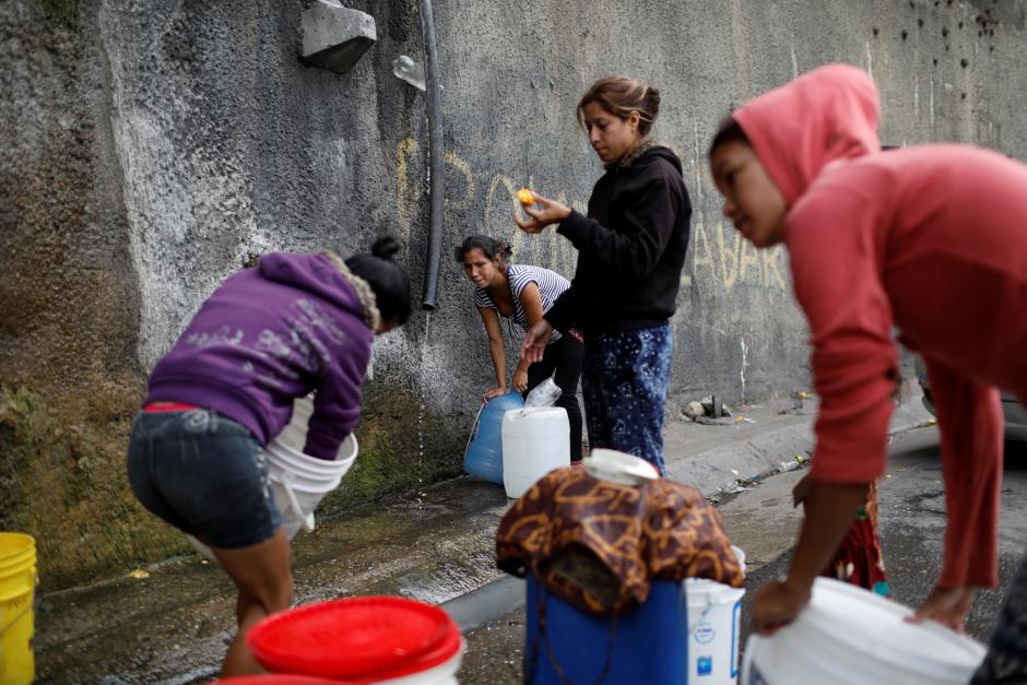 Women fill containers with water coming from a mountain, in a road at Plan de Manzano slum in Caracas, Venezuela