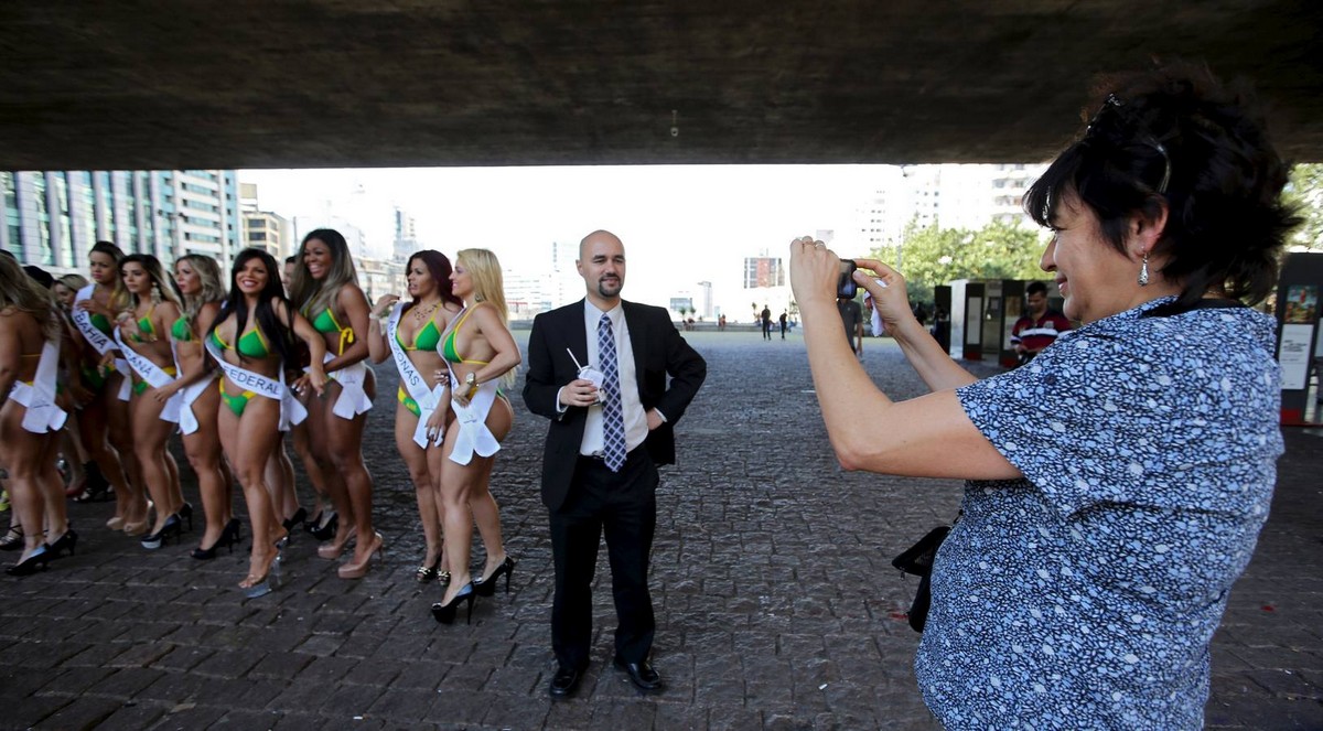 A woman takes a photo of her friend with candidates of the Miss Bumbum Brazil 2015 pageant in Sao Paulo