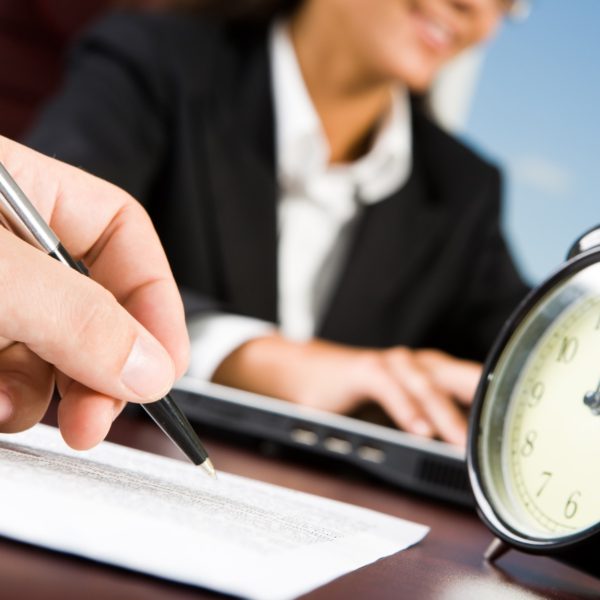 Close-up of males hand with pen over document on background of working woman