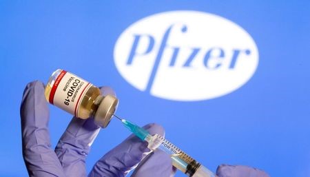 FILE PHOTO: A woman holds a small bottle labeled with a "Coronavirus COVID-19 Vaccine" sticker and a medical syringe in front of displayed Pfizer logo in this illustration taken, October 30, 2020. REUTERS/Dado Ruvic