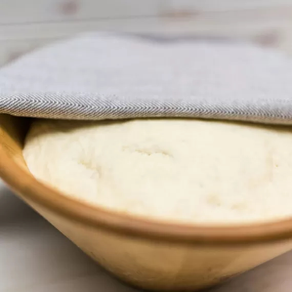 Перекладываем тесто в миску слегка смазанную растительным маслом или присыпанную мукой. Оборачиваем пищевой пленкой и укрываем полотенцем. Оставляем тесто для подъема в теплом помещении без сквозняков на 1 час.