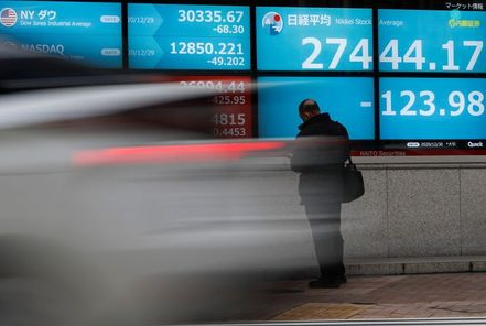 A man stands in front of a screen displaying Nikkei share average and the world's stock indexes outside a brokerage, amid the coronavirus disease (COVID-19) outbreak, in Tokyo, Japan December 30, 2020. REUTERS/Issei Kato