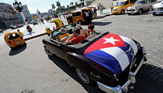 Туристы катаются на классическом американском кабриолете с кубинским национальным флагом в Гаване, Архивное фото