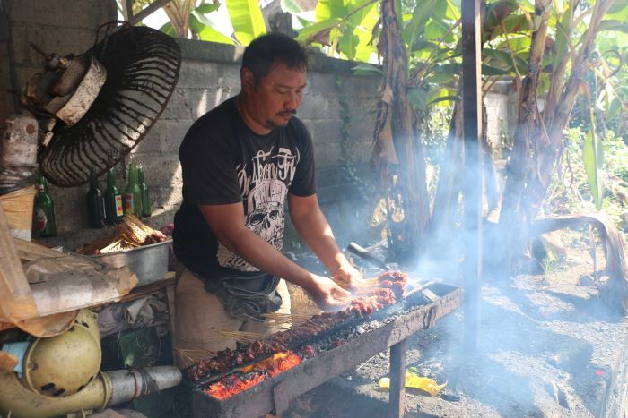 A Balinese man cooking dog-meat satay sticks