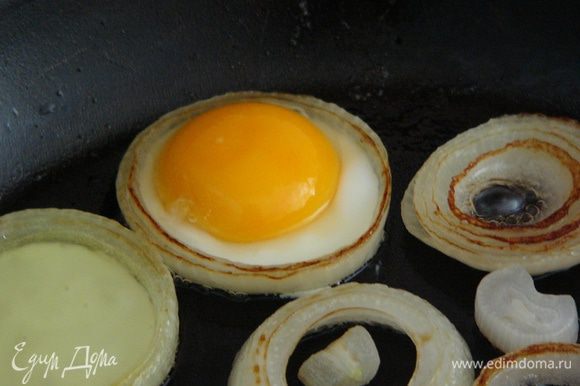 Внутрь крупных колец лука разбиваем яйцо (для удобства можно сначала разбить яйцо в чашку, убедившись, что желток не поврежден, и переложить его на сковороду ложкой). Жарить под крышкой еще пару минут, пока желток не схватится.
