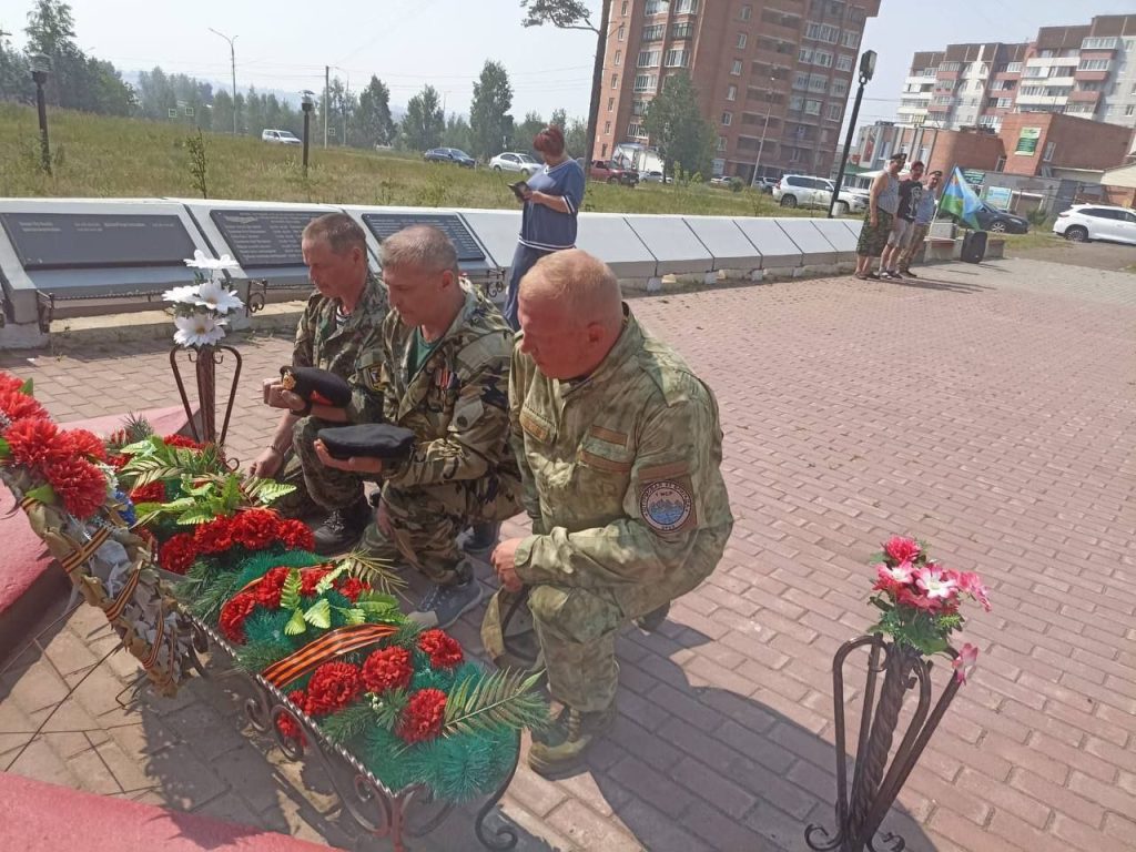 Три военных поют на мемориале с цветами.