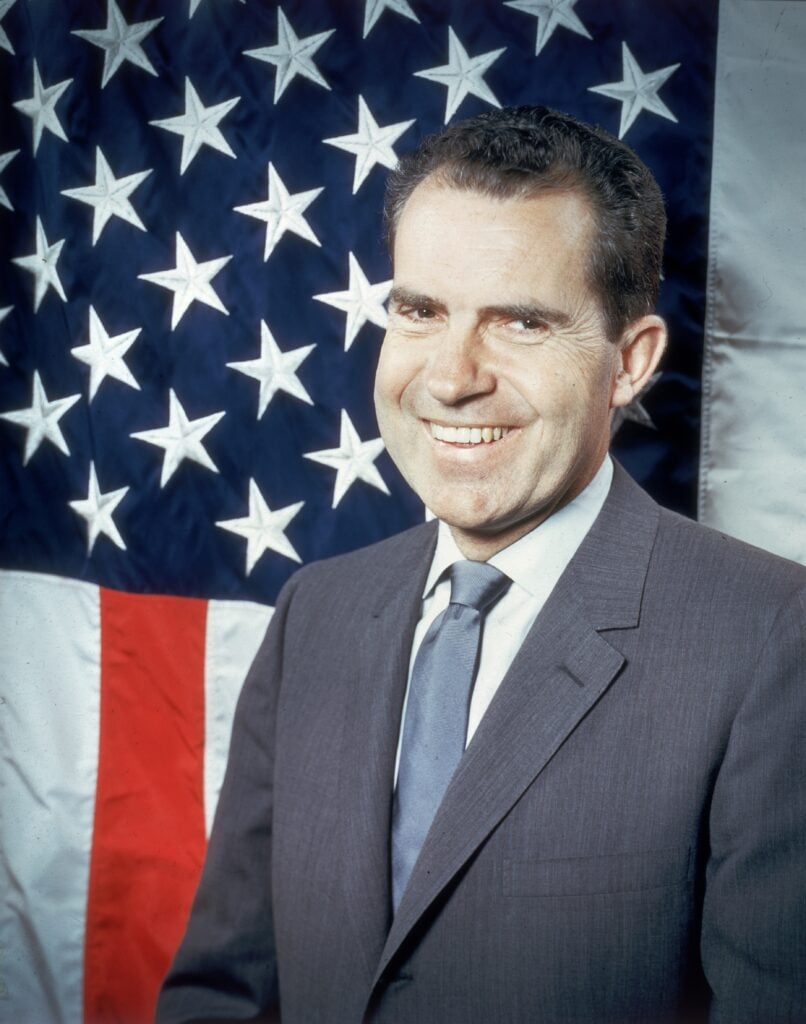 Republican presidential candidate Vice-President Richard Nixon (1913 -1994) laughing as he poses in front of the stars and stripes