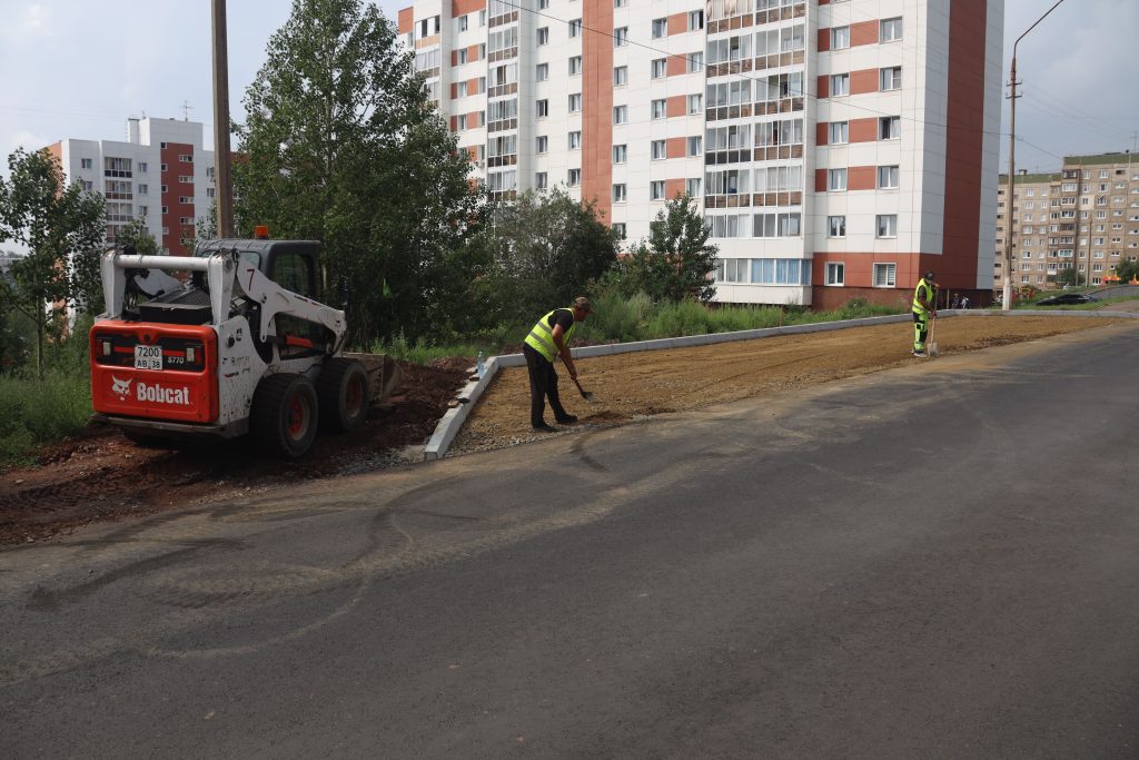 Рабочие строят тротуар возле многоквартирного дома.