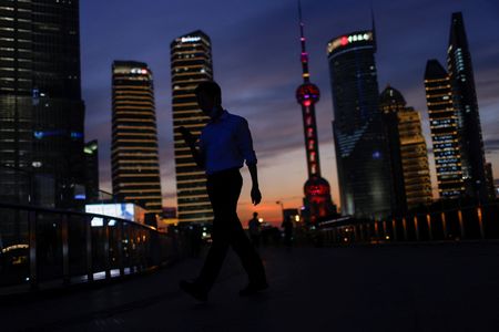 A man checks his phone while walking in Lujiazui financial district during sunset in Pudong, Shanghai, China July 13, 2021. Picture taken July 13, 2021. REUTERS/Aly Song 