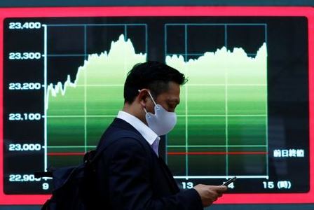 A man wearing a protective face mask walks past a screen displaying a graph showing recent Nikkei share average outside a brokerage, amid the coronavirus disease (COVID-19) outbreak, in Tokyo, Japan November 2, 2020. REUTERS/Issei Kato