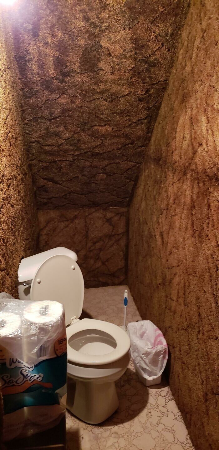 Туалет "под лестницей", в котором унитаз стоит по диагонали и частично встроен в стену (обитую ковролином)