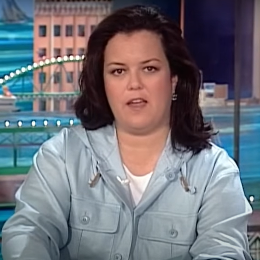 Rosie O'Donnell sits at a desk wearing a light blue shirt