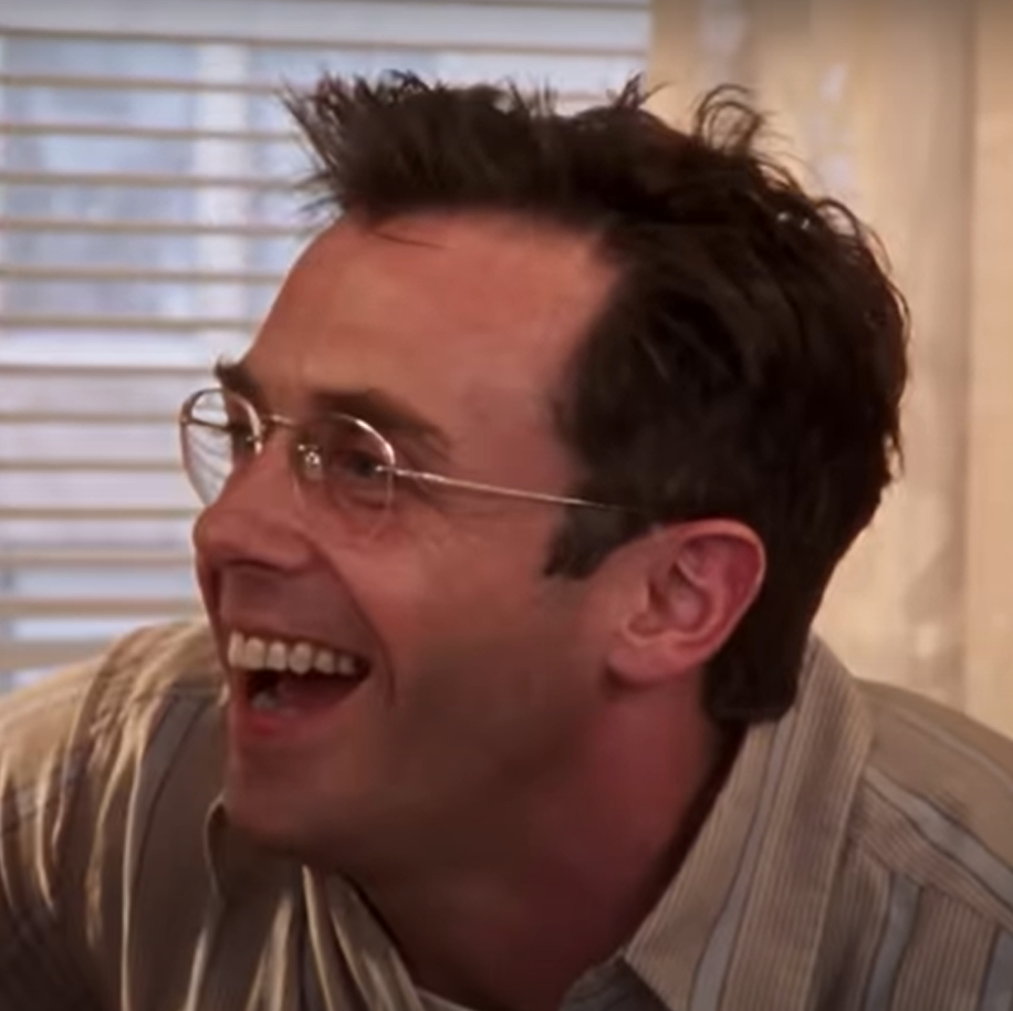 David Eigenberg as Steve Brady wears a yellow shirt and his trademark glasses and smiles