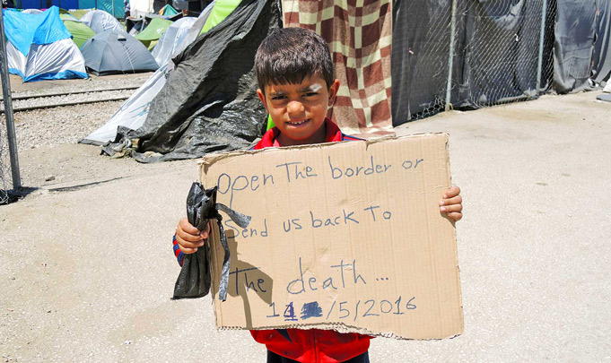 Ребенок-беженец в Греции с плакатом 