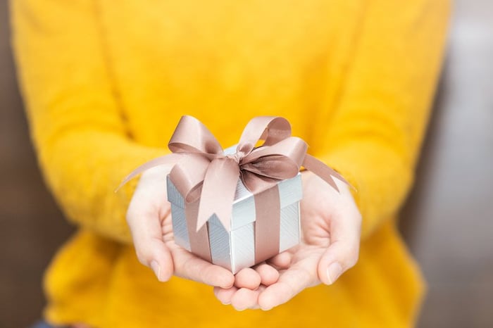 A woman in a yellow sweater holding out a wrapped gift.