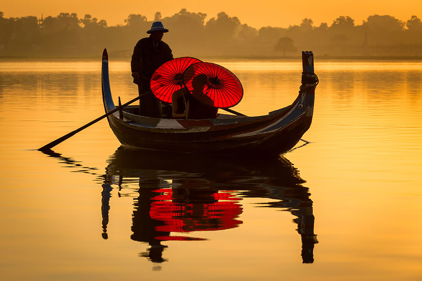 Лодка перевозит монахов с зонтами через озеро Таунгтаман