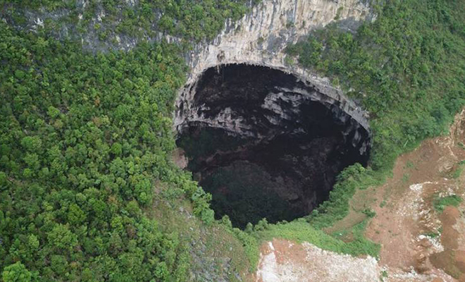 Археологи увидели гигантский провал в скалах. В пещере три входа, а на дне растут деревья высотой 40 метров