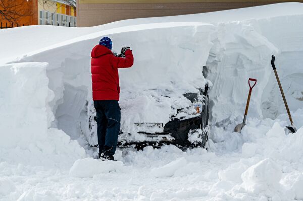 Мужчина расчищает из-под снега свой автомобиль на одной из улиц в Южно-Сахалинске