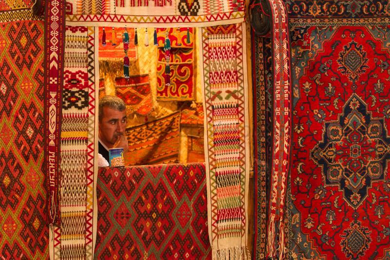 Продавец на фоне красных ковров в Узбекистане