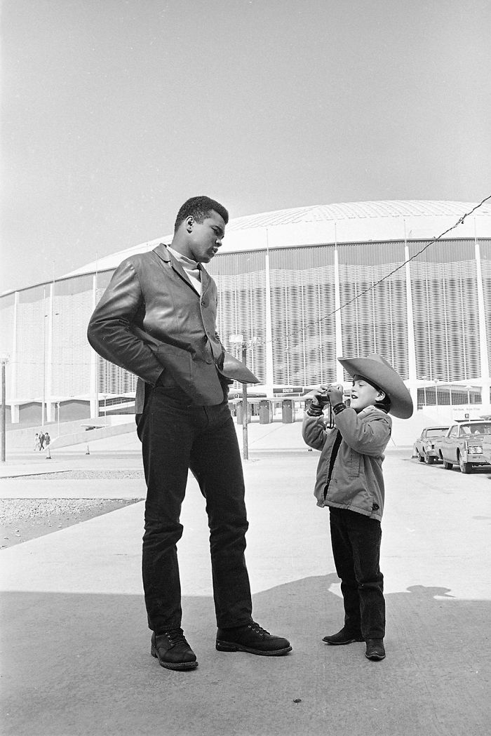 Muhammad Ali Waits Patiently As A Young Fan, Six-Year-Old Manuel De La Sierra Sets His Camera For Another Picture Outside Houston's Domed Stadium, Feb. 4, 1967
