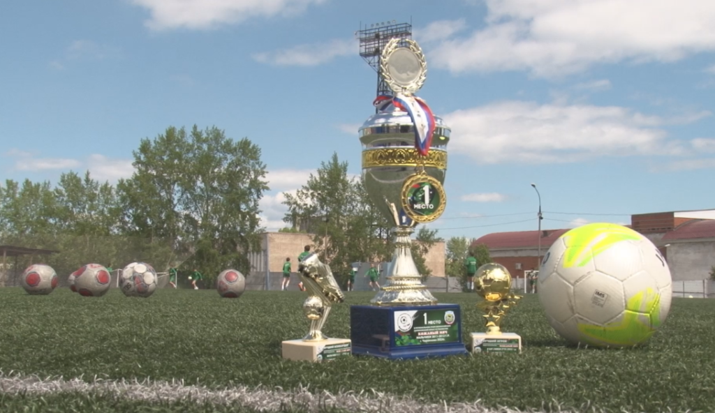 Трофеи и футбольные мячи на поле.